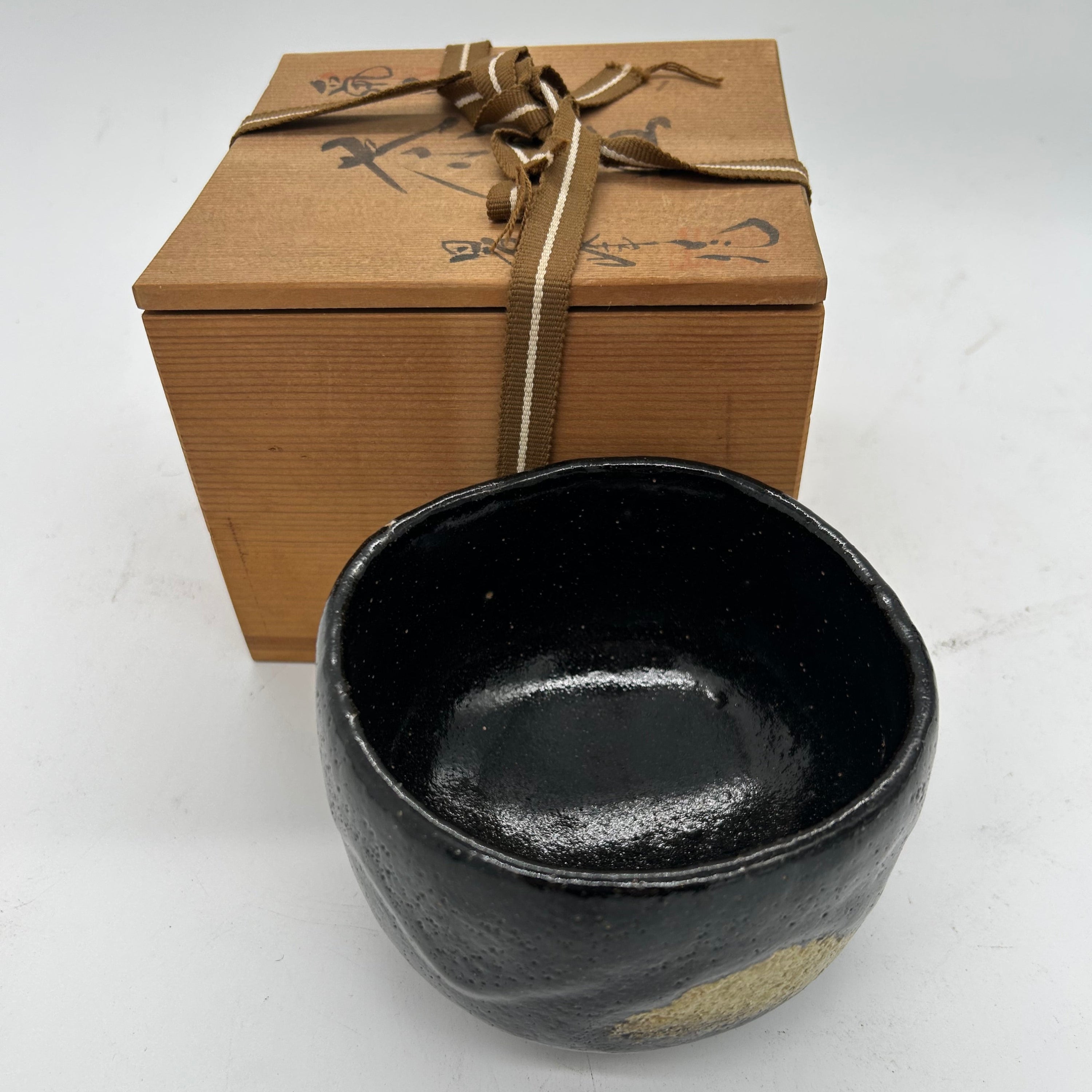 Black ceramic bowl leaning against a timber box on a white background