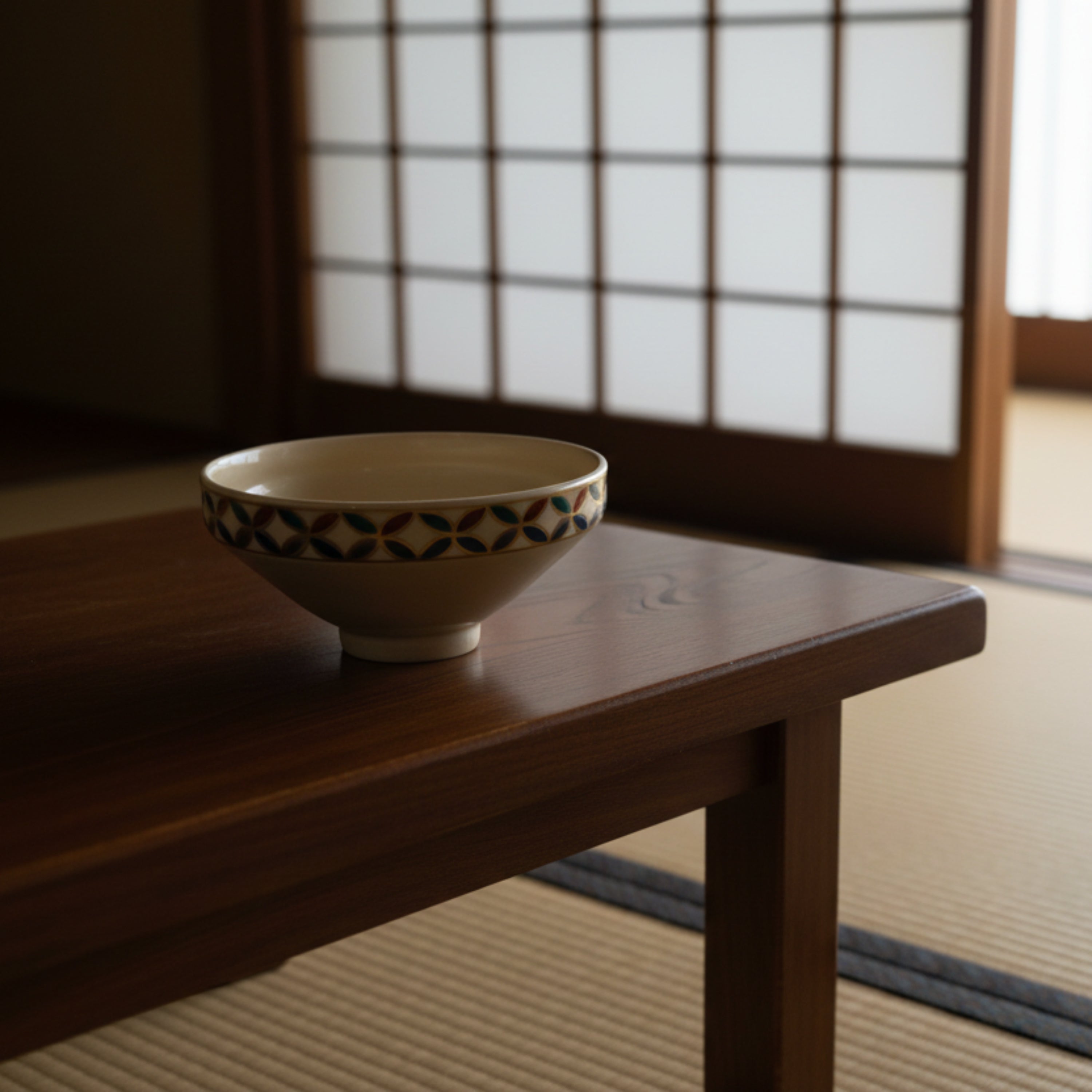 A small cream-colored ceramic bowl with a colorful decorative band of repeating leaf-like motifs in blue, green, red, and brown, photographed on a plain light background.