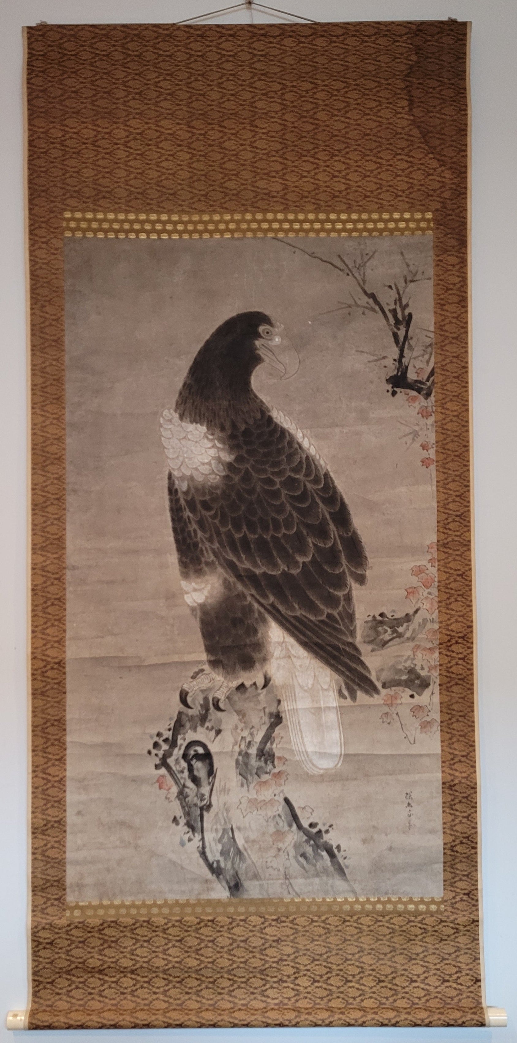 Traditional Chinese painting of a hawk on a woven scroll against a white wall.