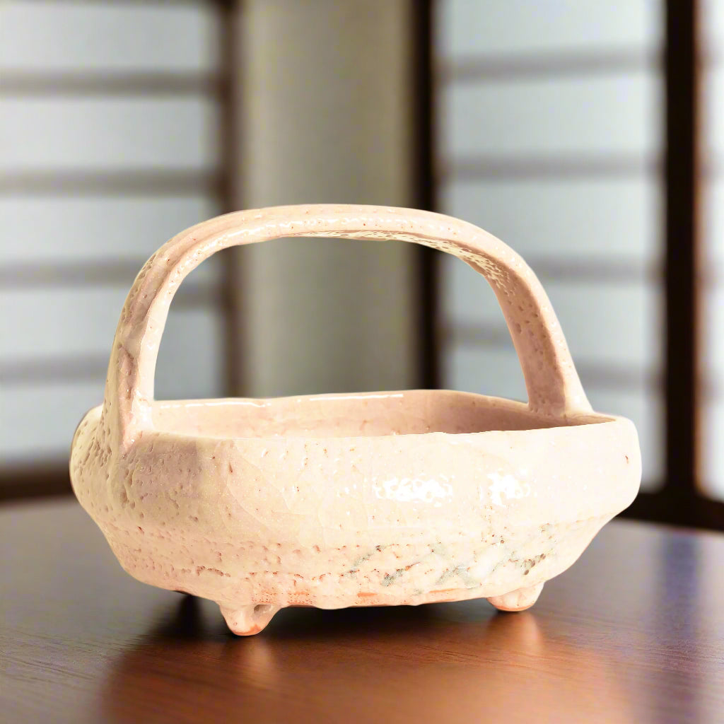 A Japanese Shino pottery bowl with handle. It has the&nbsp;distinctive&nbsp;white overglaze of traditional Shino ware, with a subtle pink undertone showing through from the clay. A frond-like design in black wraps around the inside of the bowl.
