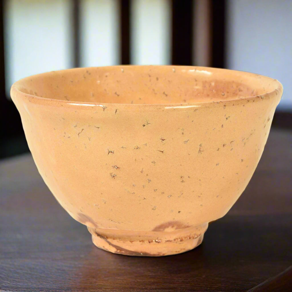 A Japanese pottery tea bowl with an organic shape and feel. The pink clay is glazed and textured. It has a maker's stamp on the base.