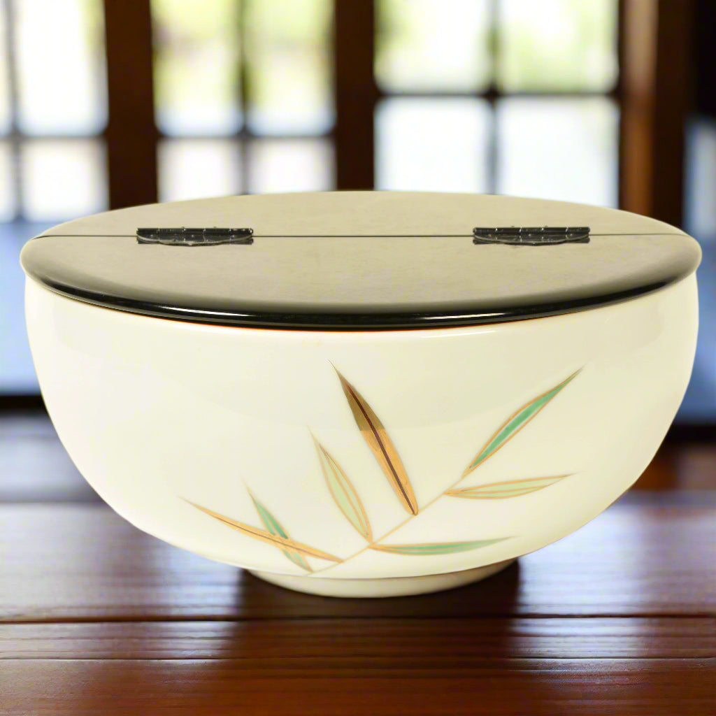A vintage Japanese porcelain mizusashi, a water pot used for tea ceremony, with a black lacquer hinged lid. It has a hand painted and gilded design of bamboo leaves. c.1970's.