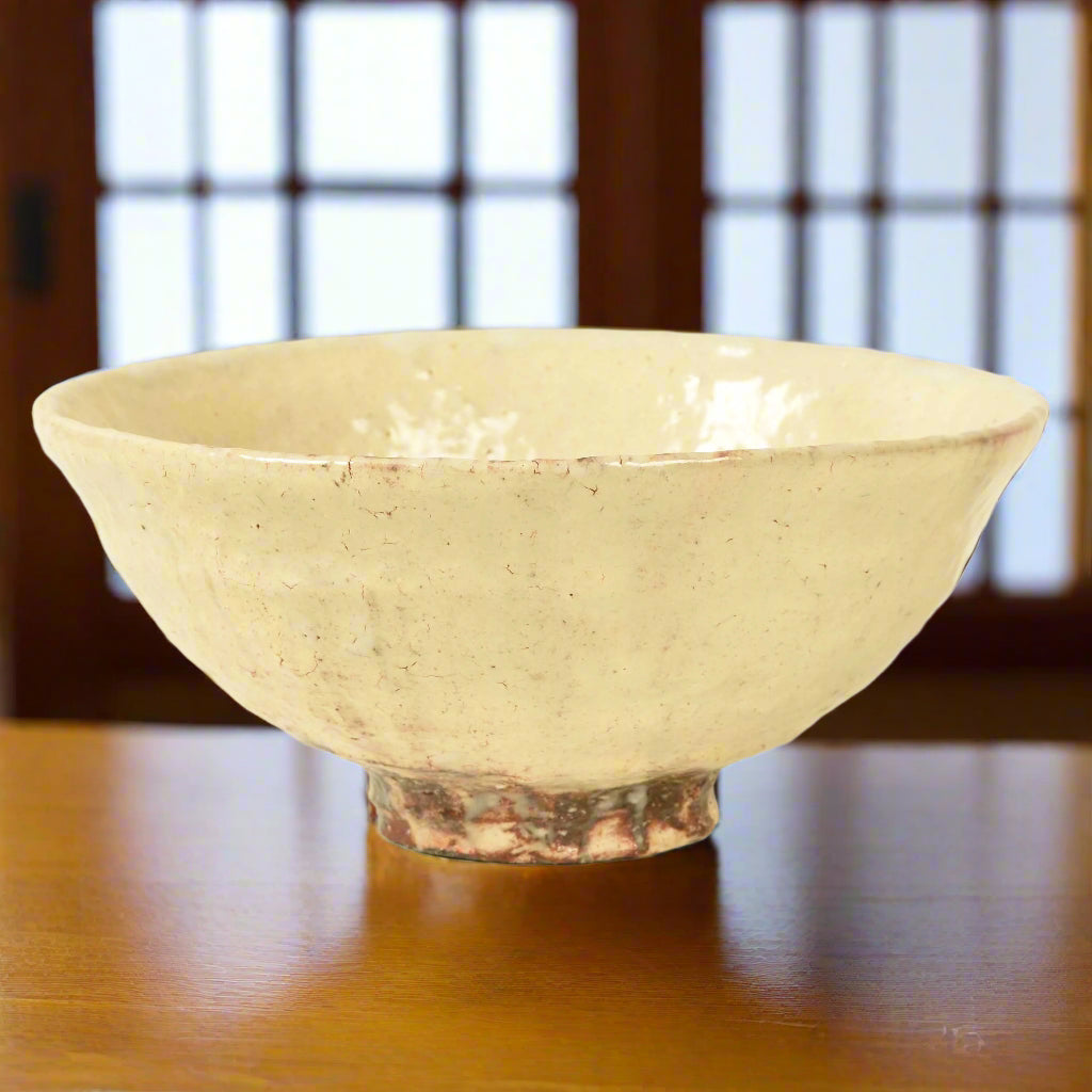 A Japanese pottery tea bowl with an organic shape and feel, it's white glaze dripping unevenly over the red brown clay which shows through at the base and interior.
