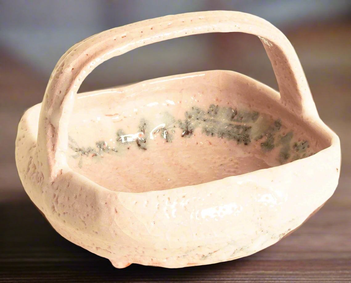 A Japanese Shino pottery bowl with handle. It has the&nbsp;distinctive&nbsp;white overglaze of traditional Shino ware, with a subtle pink undertone showing through from the clay. A frond-like design in black wraps around the inside of the bowl.